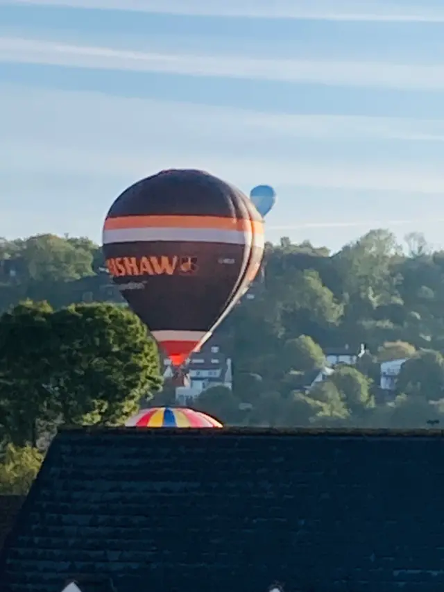 Three balloons pass over rooftops and trees.