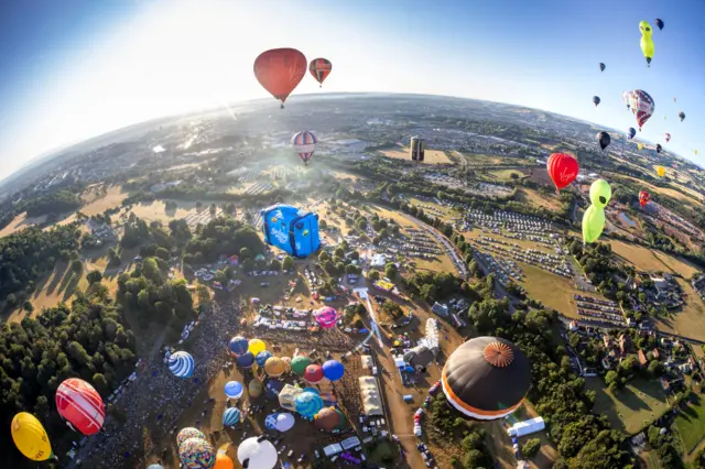 An aerial view of the entire site of the Bristol Balloon Fiesta showing multiple balloons in the air or being inflated ready to take off