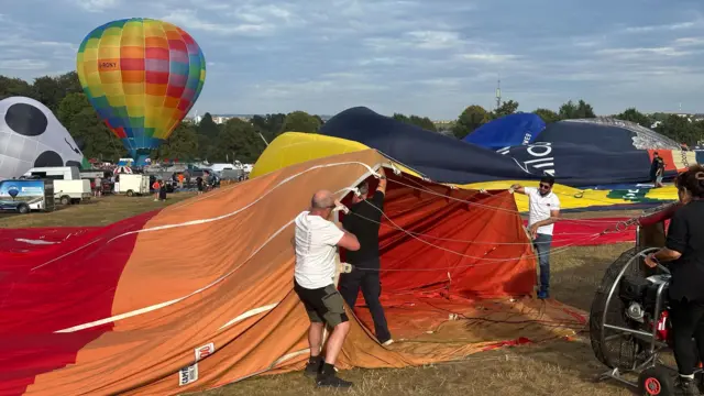 Three men hold the canopy of a hot air balloon as it is inflated