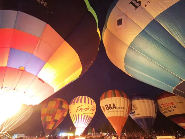 A close-in view of some hot air balloons being lit up by their burners on a dark night