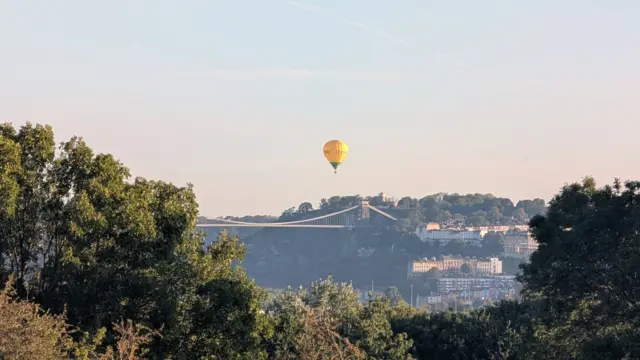 A yellow and green hot air balloon hovers in the dusky sky over Clifton Suspension Bridge
