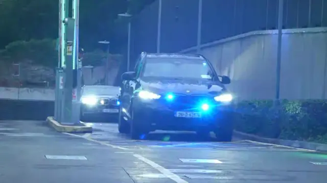 Black cars with flashing blue lights seen leaving an underground car park.