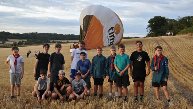 A group photo of boy scouts in a field with a landed hot air balloon behind them.