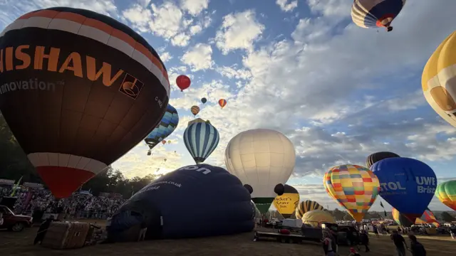 Balloons are in the sky while some are inflating on the ground.