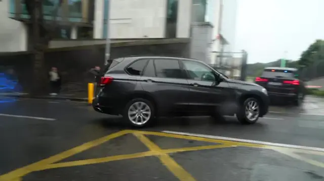 Two cars stream through the gates by the court