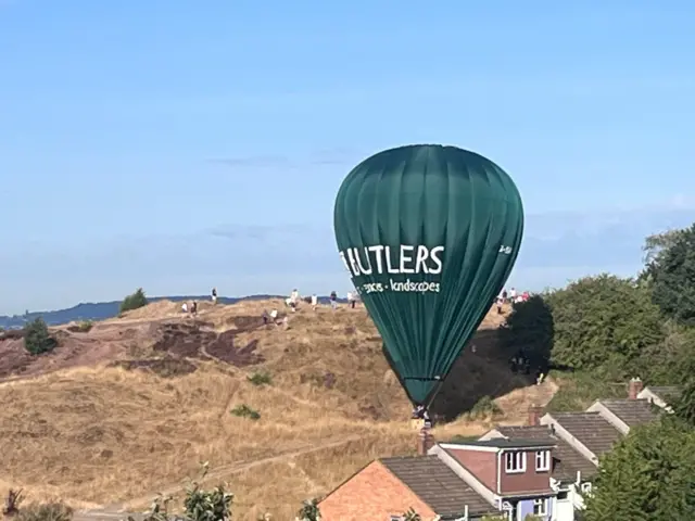 A green hot air balloon has landed on a hill behind some houses.