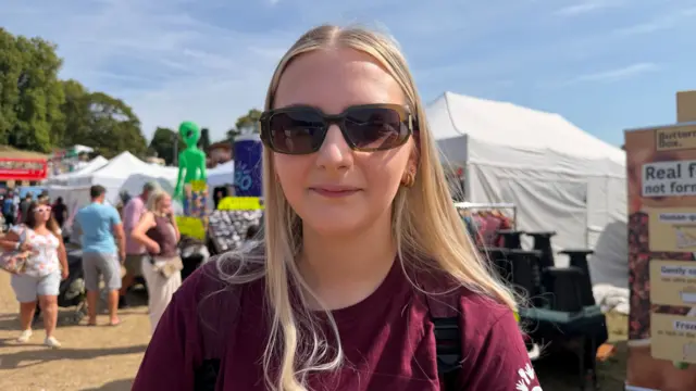A woman is wearing a burgundy T-Shirt and sunglasses.