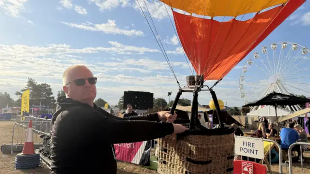 A man in a black hoodie is holding a model hot air balloon.