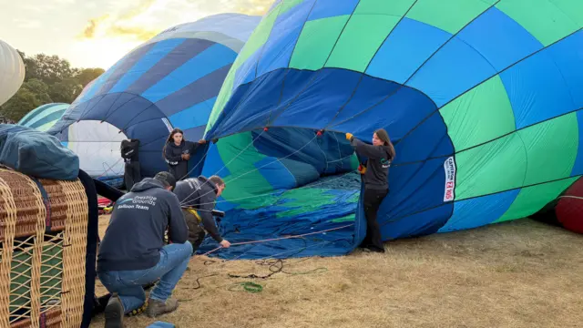 People are in the process of getting up a hot air balloon on the ground.