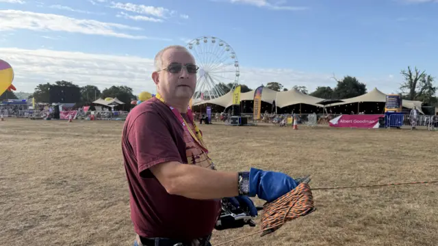 A man is standing on a field holding on to a rope. He is wearing sunglasses and a red T-Shirt.