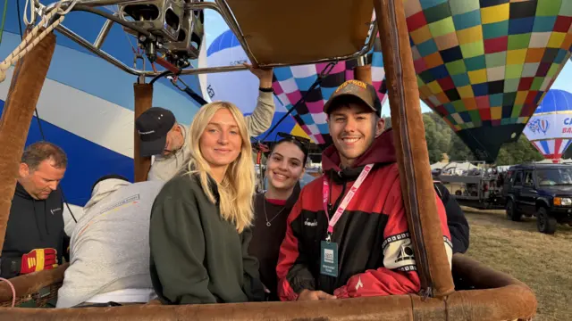 People are standing in a balloon basket on the ground.