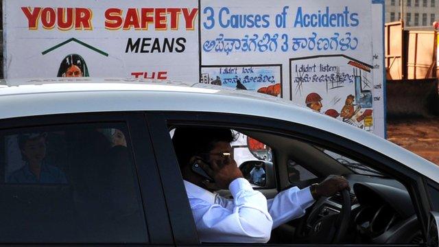 An Indian man talks on his mobile phone as he drives past a traffic awareness poster on a busy road in Bangalore