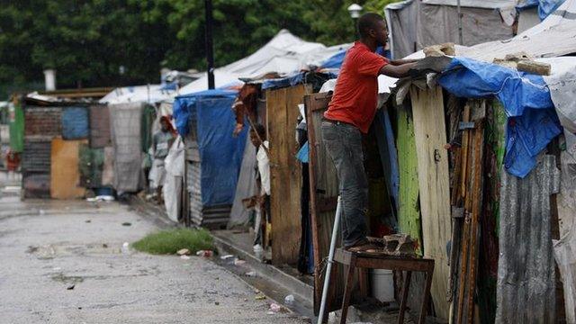 A Haitian earthquake survivor reinforces his tent, under the rain, at a provisional camp