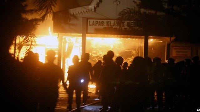 Police officers stand outside Tanjung Gusta prison, on fire