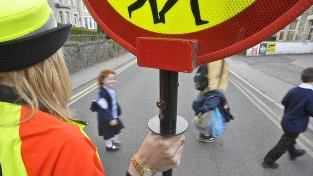 Children crossing the road with the help of a lollipop lady