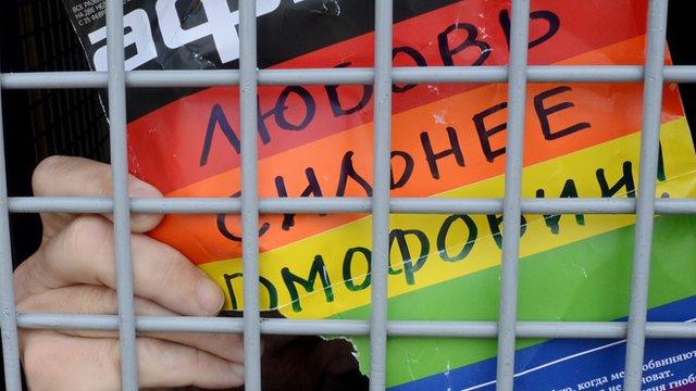 Gay activist in police van with sign saying Love is stronger than Homophobia, 25 May 13