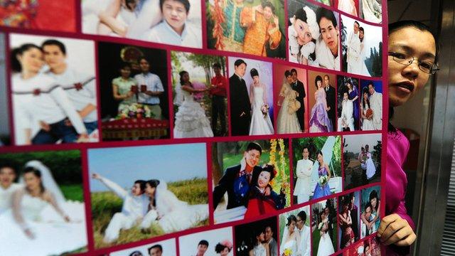 Gong Haiyan poses beside a poster in her Beijing office of photographs of married couples who met on her website (file photo)