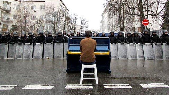 Man playing piano in front of line of riot police