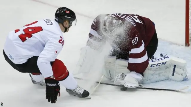 Canada forward Corey Perry skids to a stop as Latvia goaltender Kristers Gudlevskis smothers the puck