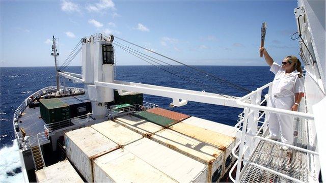 RMS St. Helena Second Officer Mia Henry holds the Queen's Baton aloft looking out over the RMS St. Helena