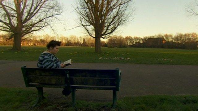 Woman sat reading on park bench