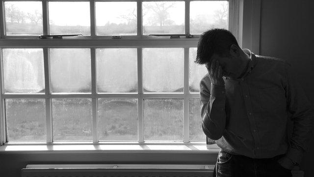 A man stands by a window with his head in his hands