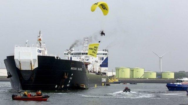 A member of Greenpeace in a hang-glider, carrying a banner over the Russian oil tanker