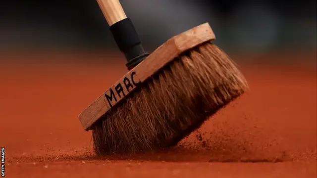 A member of the ground staff sweeps the red clay with his broom called Marc