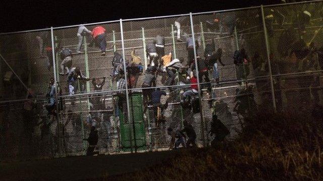 Sub-Saharan migrants scale a metallic fence that divides Morocco and the Spanish enclave of Melilla