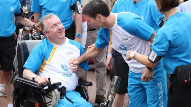 Baton bearer in wheelchair shakes hand of next baton bearer.