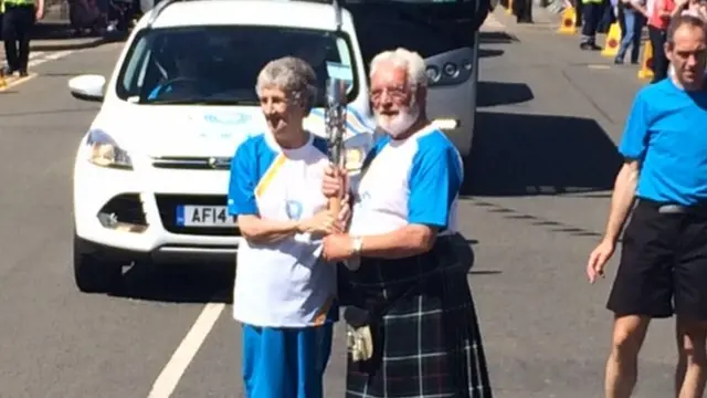 Woman hands baton to man in kilt