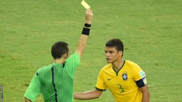 Turkish referee Cuneyt Cakir shows a yellow card to Brazil"s defender Thiago Silva