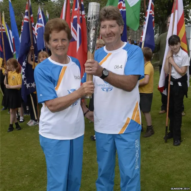 Eileen Legg hands the Glasgow 2014 Queen's Baton to Batonbearer 064 Geoff Legg through Castle Douglas in Dumfries & Galloway.