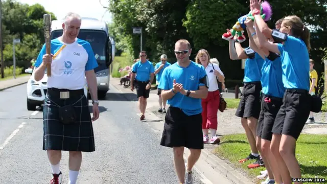 Daniel Gibbons gets some support from the security team during his moment with the baton in Mossblown