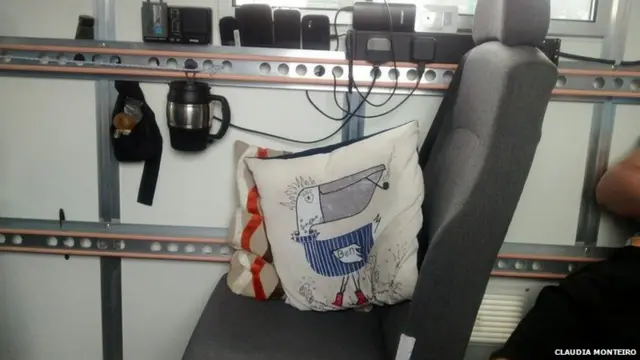 Inside of van. A coffee mug hangs from the side rail, and a couple of scatter cushions rest on a seat.