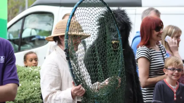 Woman wearing pith helmet holding a giant comedy net stands next to a person in a gorilla costume