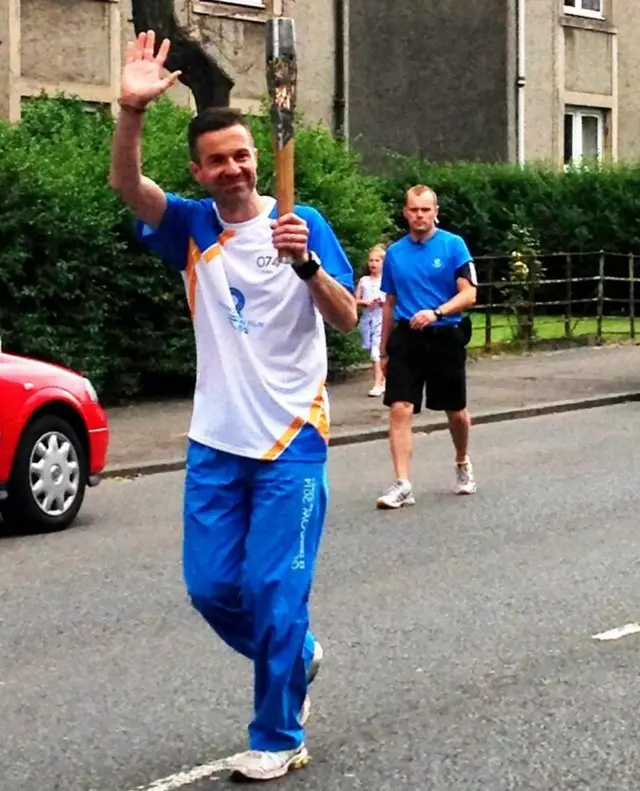 Stephen Rooney waves as he runs with baton