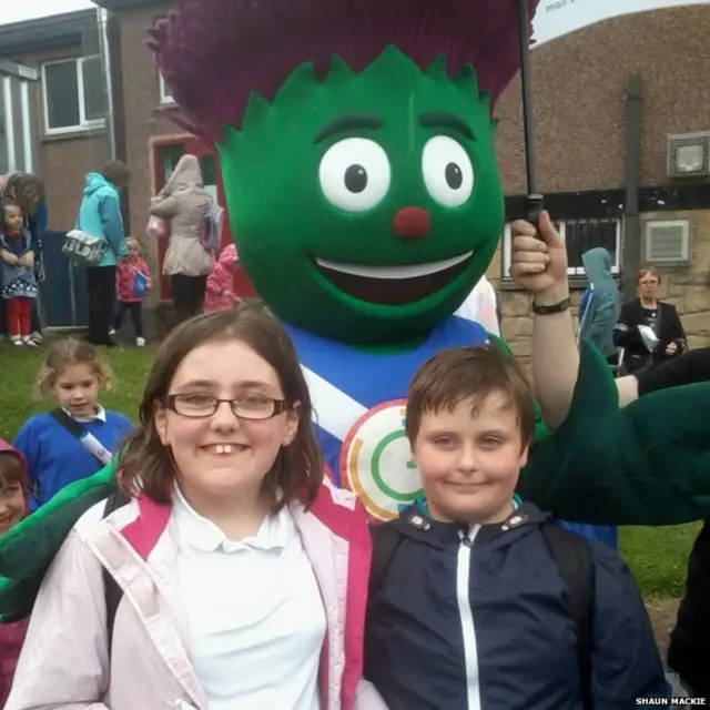 Two children stand in front of Commonwealth Games mascot Clyde