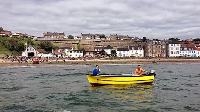 Two men in a small boat, one of whom is holding a small dog