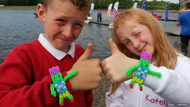 Boy and girl give thumbs up. Both are wearing loomband bracelets that resemble Games mascot Clyde.