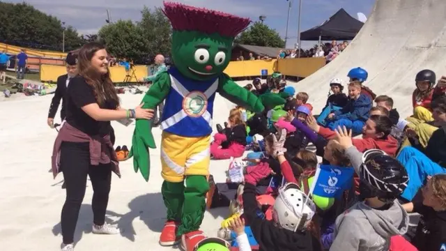 Games mascot Clyde high-fives small children at a dry ski slope.