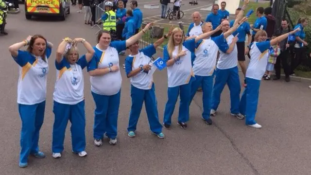 Group of baton bearers, some of whom are doing Mo Farah's 'mo-bot' while others are copying Usain Bolt's trademark point.