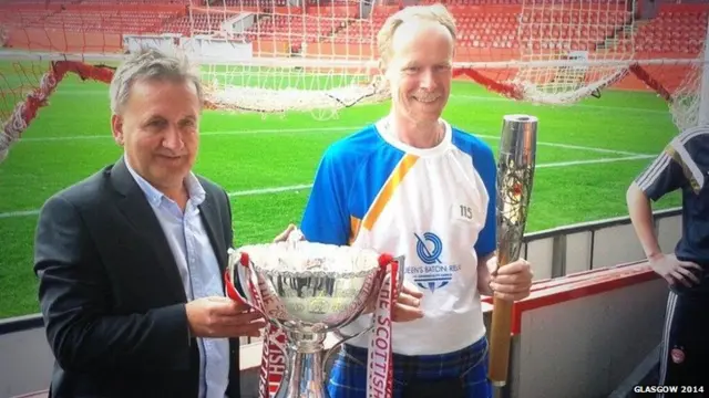 Baton bearer poses with Scottish football league cup and baton