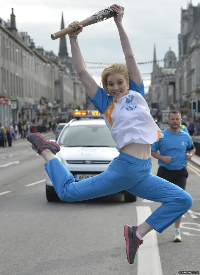 Rebecca Bee leaps in the air while holding Queen's baton.