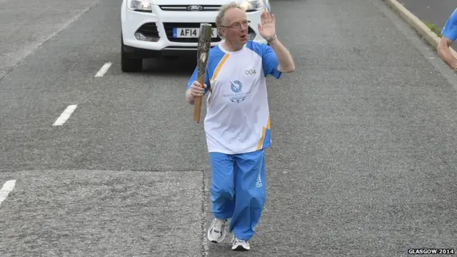 Iain Jamieson waves as he carries Queen's baton