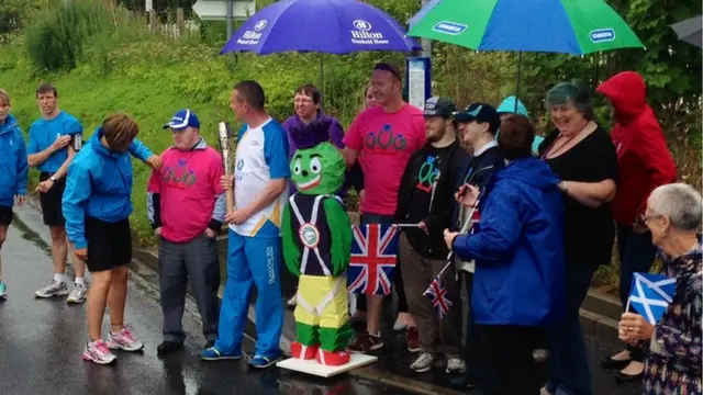 Baton bearer George Law takes shelter under an umbrella