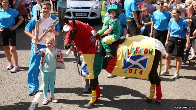 Baton bearer poses next to horse and rider, both of whom are covered in Glasgow 2014 apparel.