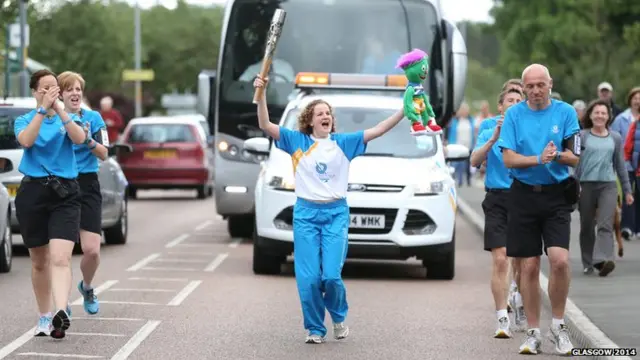 Marian Wyllie runs with baton, while holding a miniature Clyde mascot aloft