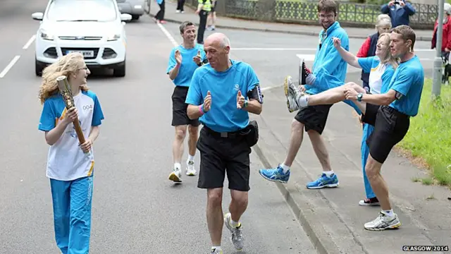 Police escorts and previous baton bearer dance can can as current baton bearer looks on.