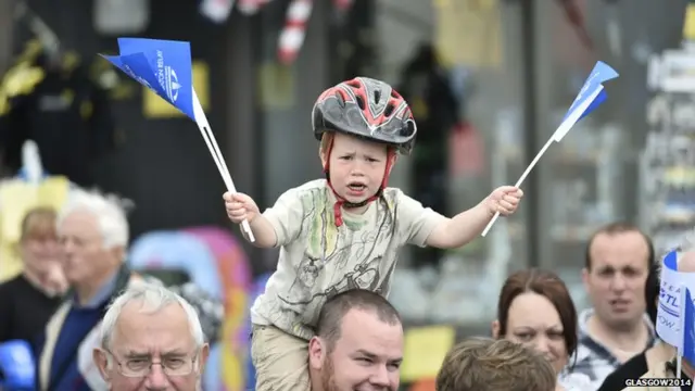 Small boy on man's shoulders waving two flags